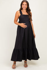woman wearing a black maternity maxi dress with ruffled straps and a flowing skirt, holding her baby bump