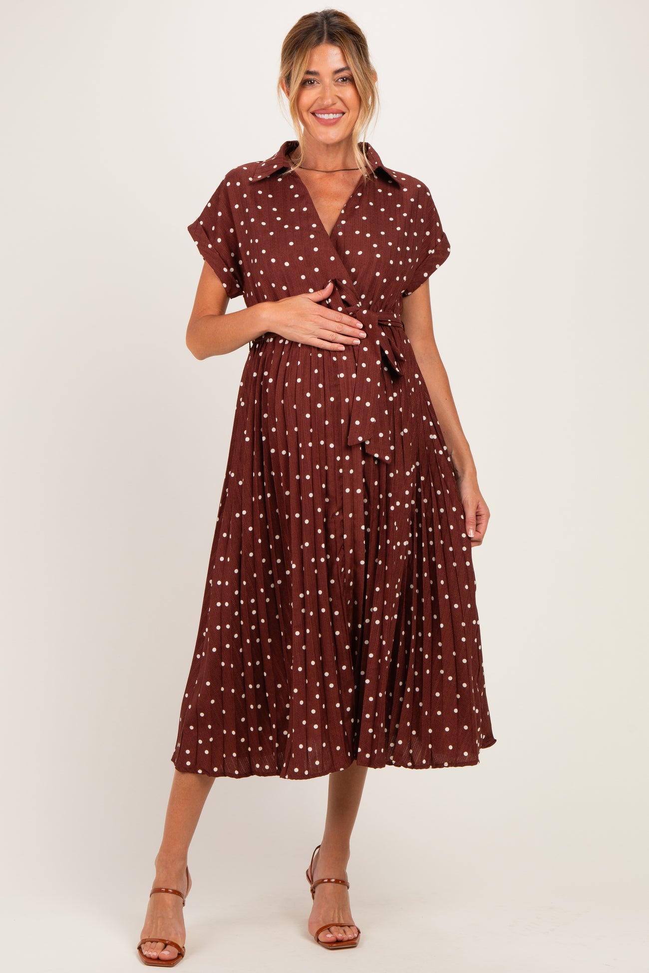 woman wearing a brown polka dot maternity dress with a tie waist and short sleeves, holding her baby bump