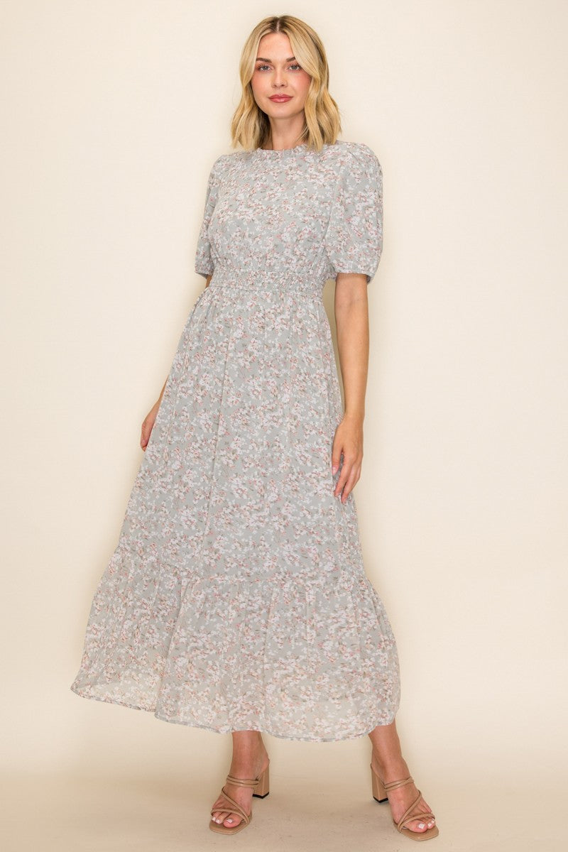 woman wearing a light grey floral maxi dress with puff sleeves and a tiered skirt, paired with strappy sandals