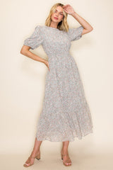 woman wearing a light gray floral midi dress with puff sleeves and a smocked waist