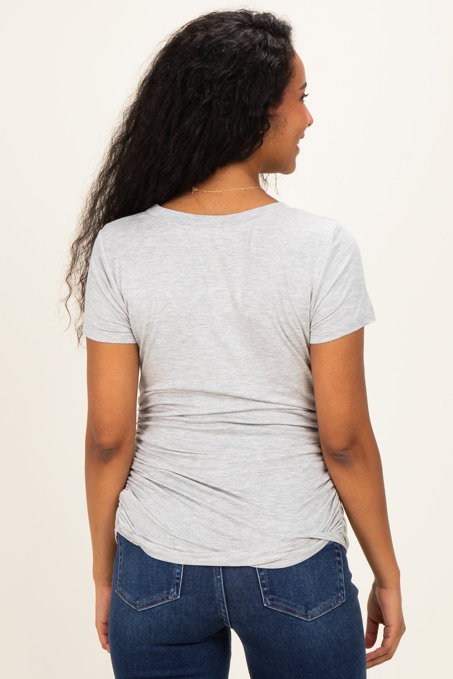 woman wearing a light gray short sleeve maternity top with gathered side details, showing her back