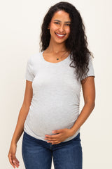 woman wearing a light gray short sleeve maternity top and gently holding her baby bump