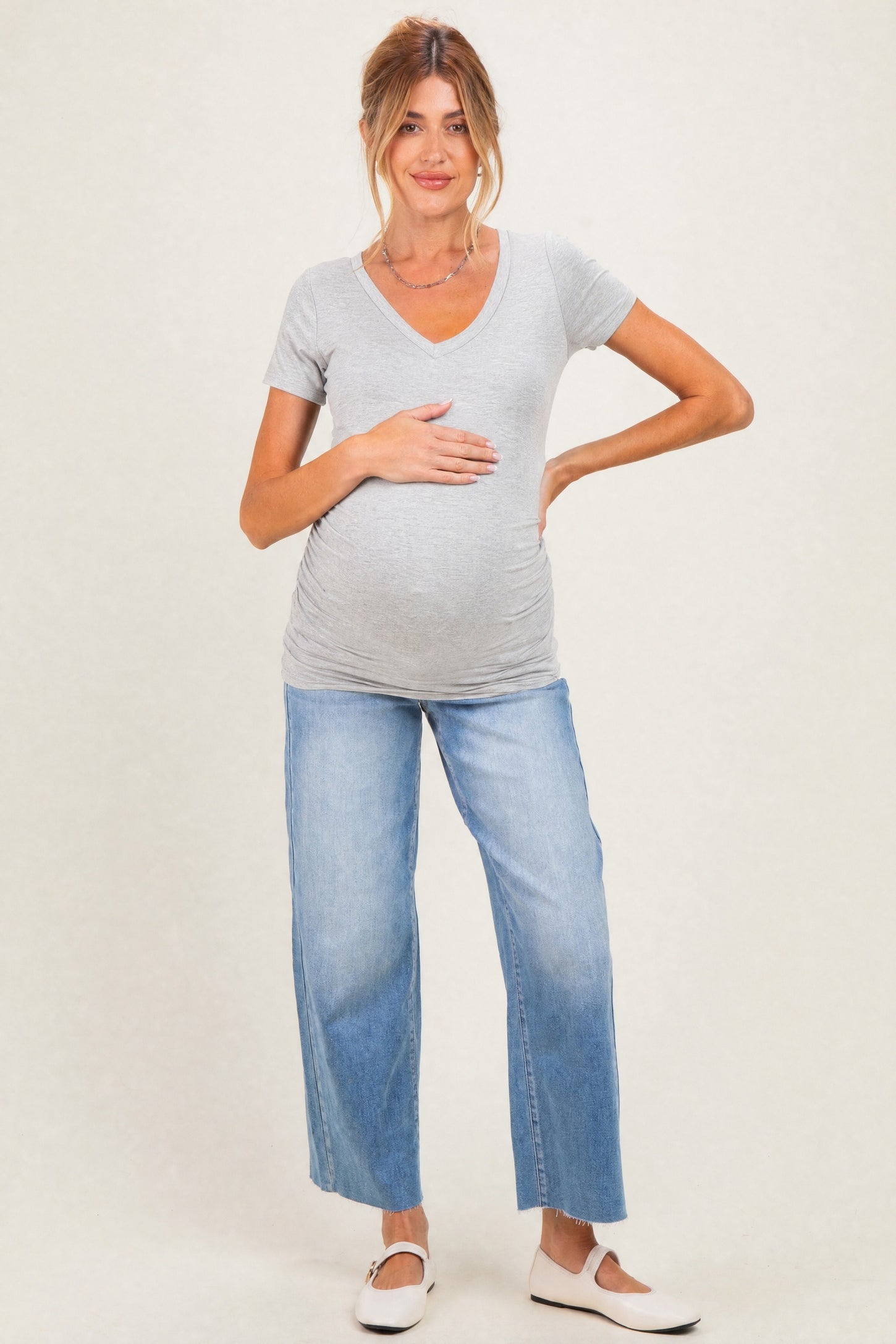 woman wearing a gray v-neck maternity t-shirt and distressed light wash jeans, holding her baby bump