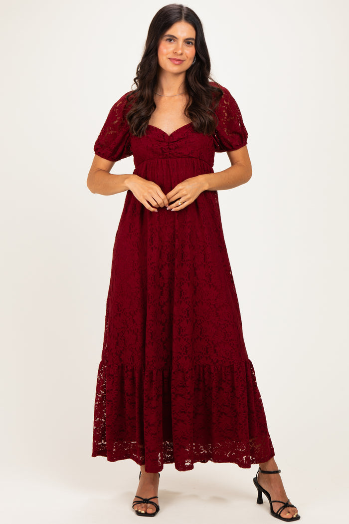 woman wearing a burgundy lace maxi dress with short sleeves and a tiered hem, standing in a neutral background