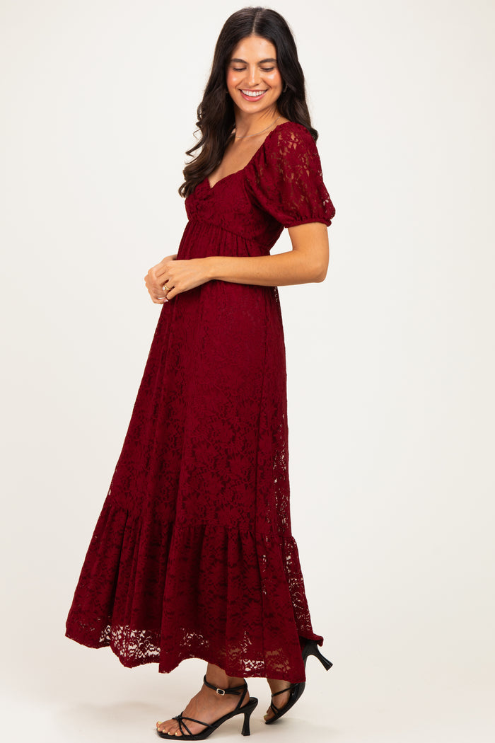 woman wearing a burgundy lace maxi dress with puff sleeves and a tiered hem, smiling to the side