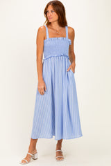 woman wearing a light blue striped midi dress with smocked bodice and pockets, standing on a beige background