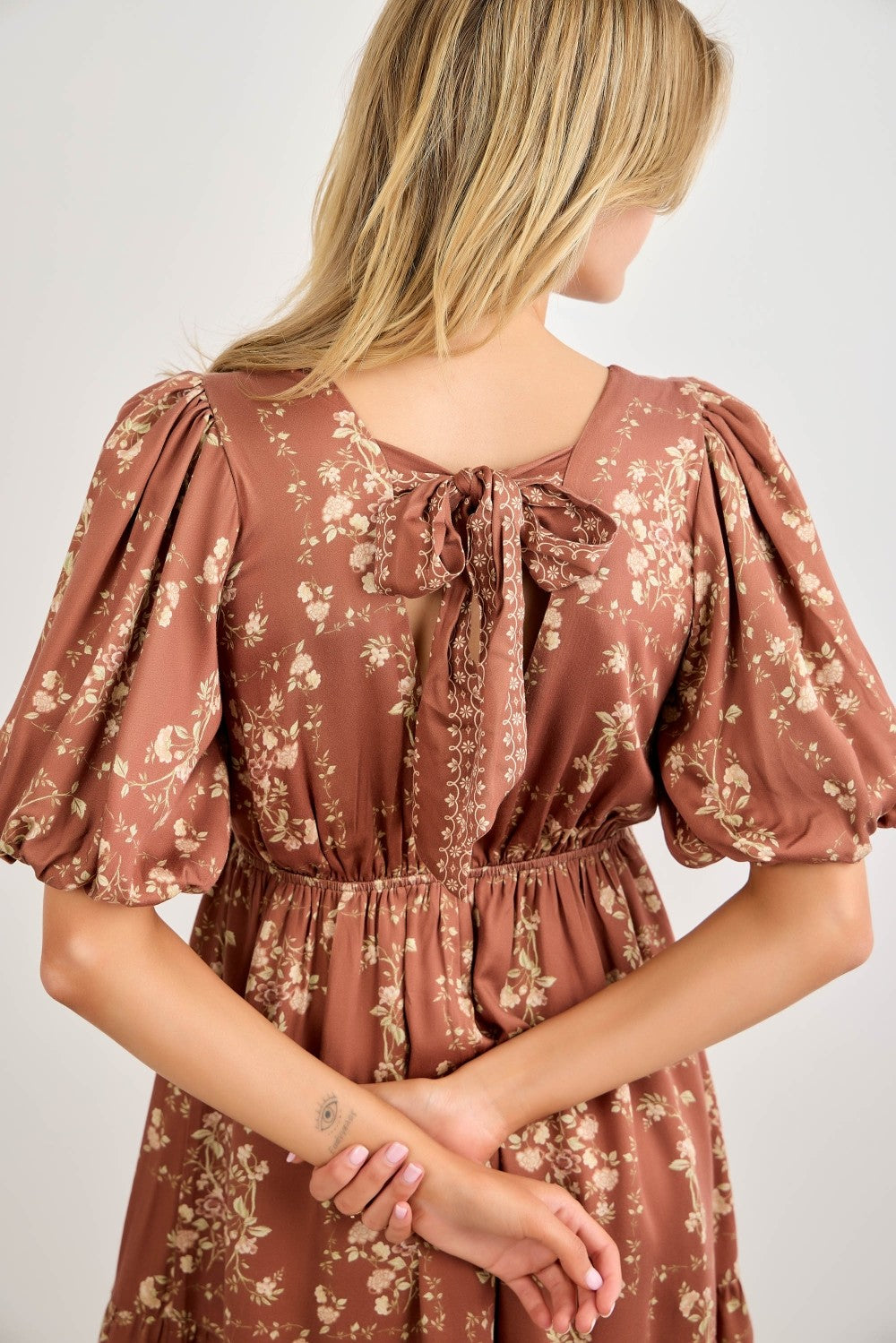 woman wearing a brown floral puff sleeve dress with a back tie detail and cinched waist