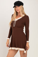 woman wearing a brown long sleeve ribbed dress with cream trim and a tie neckline, paired with a black cap