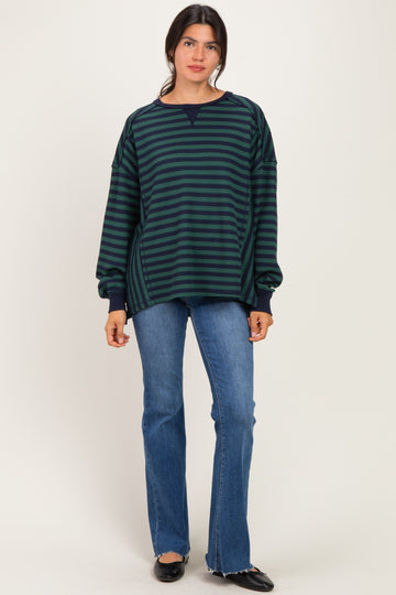 woman wearing a navy and green striped oversized sweatshirt with a crew neck and long sleeves, paired with flared jeans