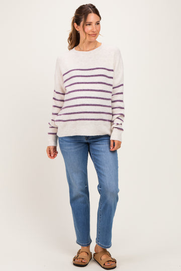 woman wearing a cream striped maternity sweater with purple lines and blue jeans