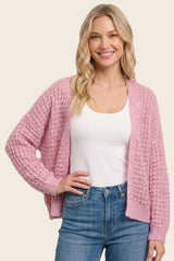 woman wearing a light pink open-knit cardigan over a white tank top and blue jeans