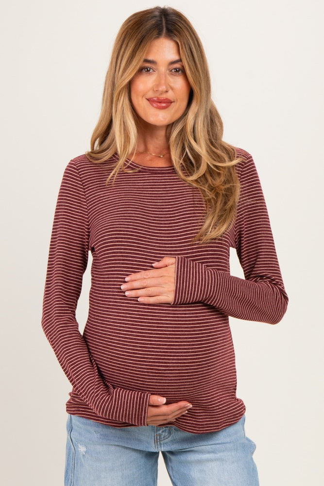 woman wearing a burgundy and white striped maternity long sleeve top and holding her baby bump