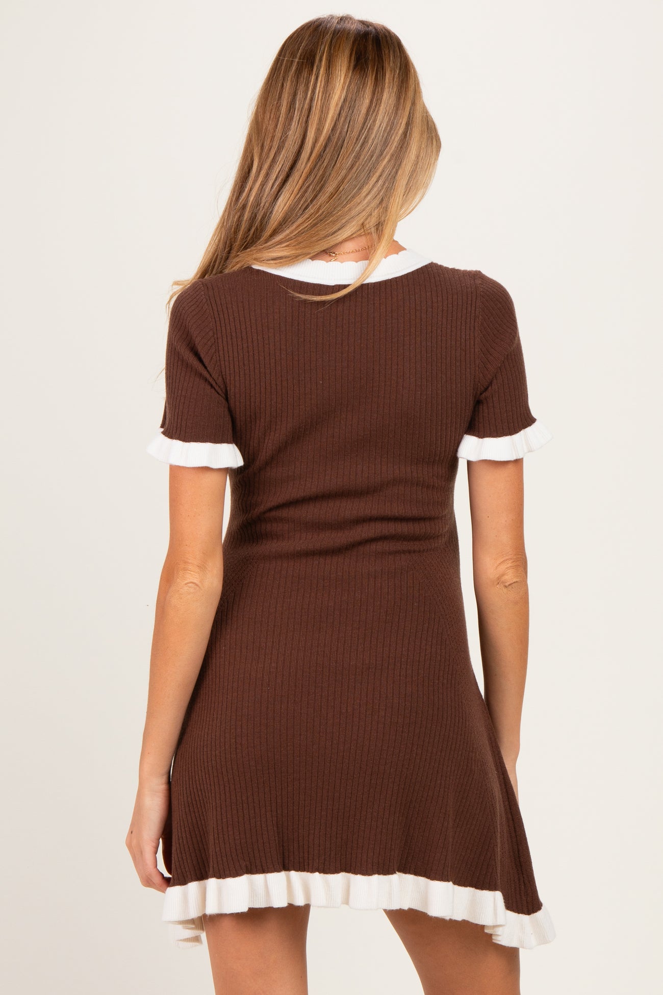 woman wearing a brown maternity dress with white ruffle trim and short sleeves, showing the back view