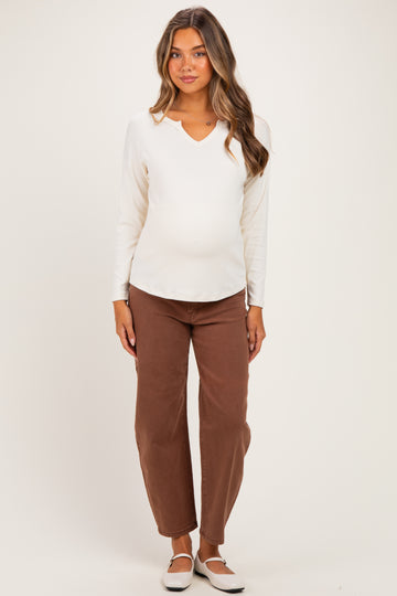 woman wearing a white ribbed long sleeve maternity top and brown wide-leg pants, showing her baby bump