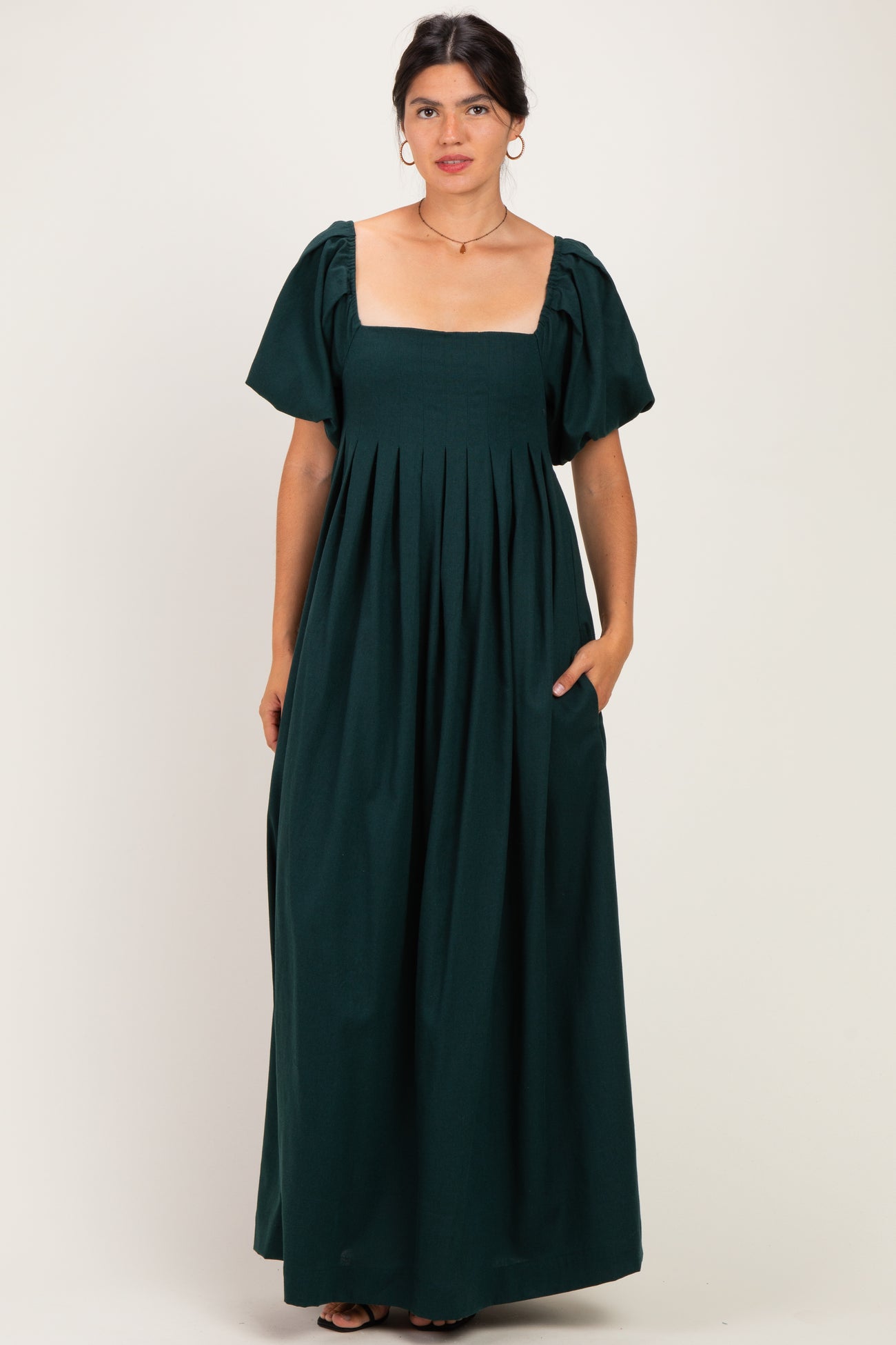 woman wearing a dark green maxi dress with a square neckline, short puff sleeves, and side pockets