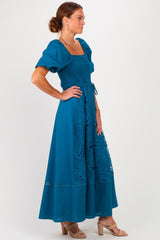 woman wearing a teal maxi dress with puff sleeves and lace detailing, standing in profile
