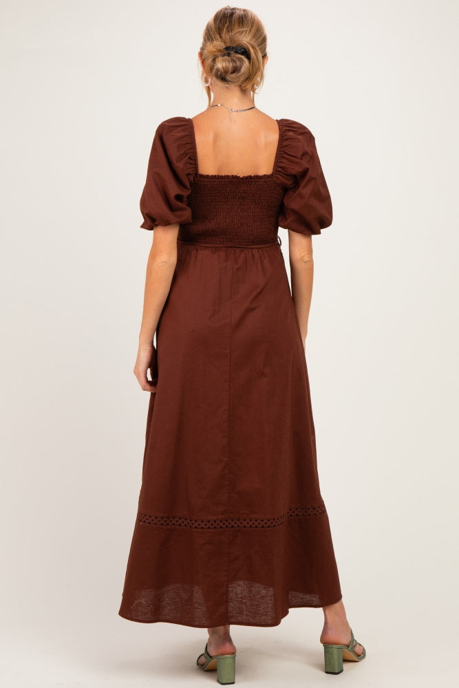 woman wearing a brown maternity maxi dress with puff sleeves and smocked bodice, showing the back view