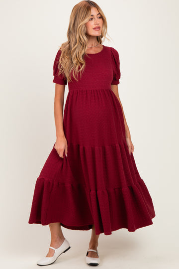 woman wearing a burgundy maternity dress with puff sleeves and ruffled hem, featuring a visible baby bump
