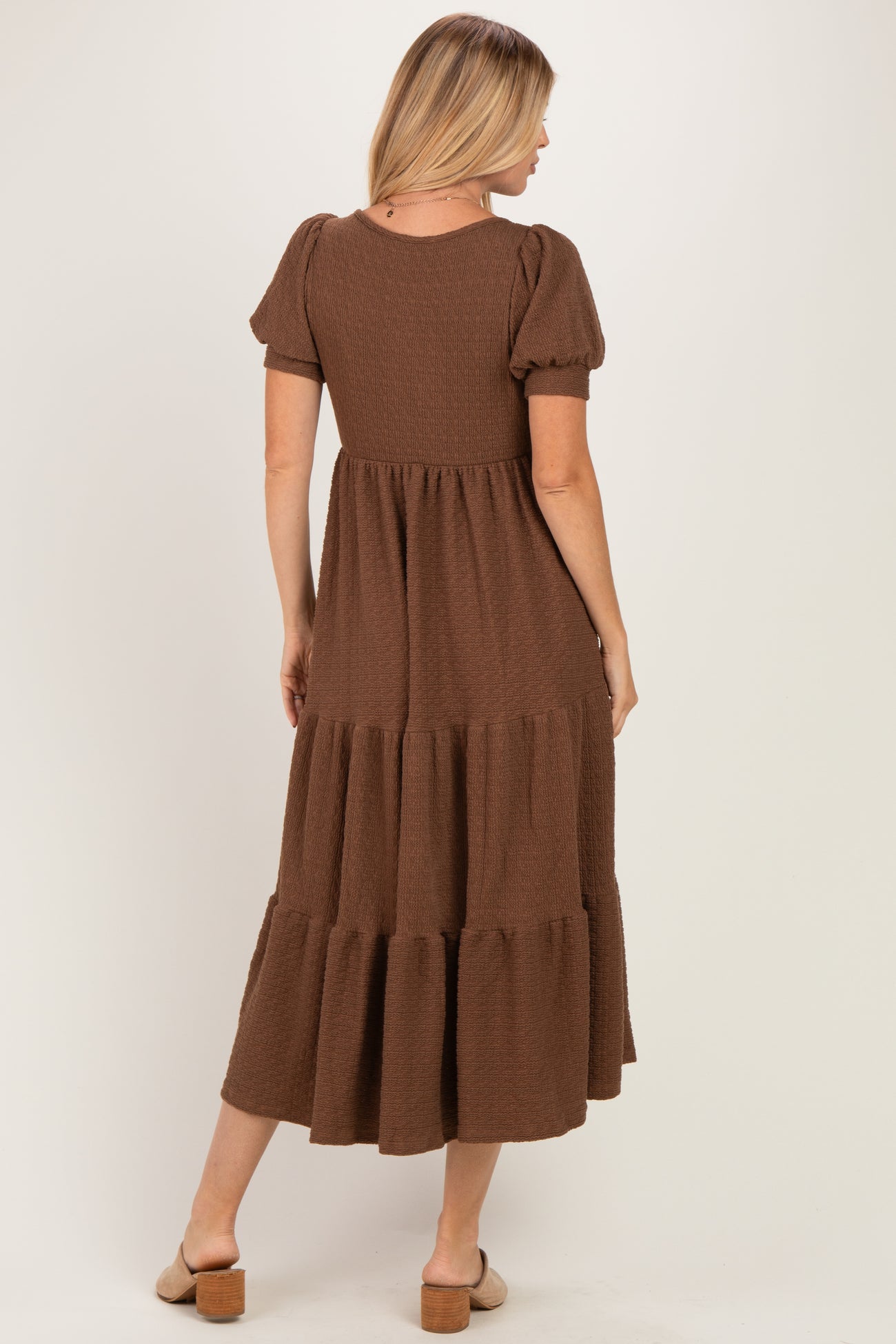 woman wearing a brown tiered maxi dress with short puff sleeves, standing and showing the back view