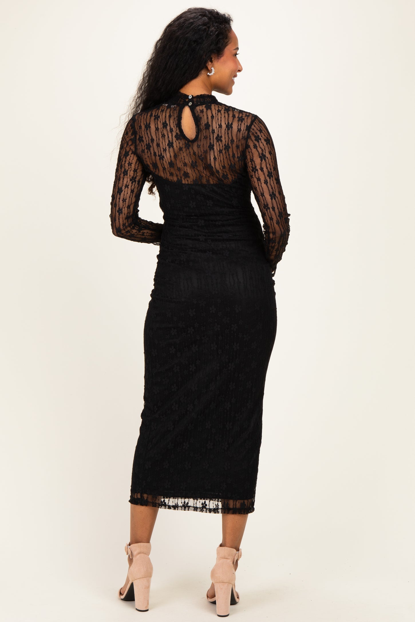 woman wearing a black maternity dress with lace details and long sleeves, showing a keyhole back design