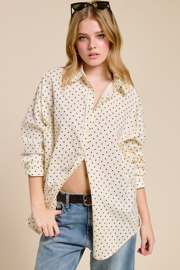 woman wearing a cream button-up shirt with black polka dots and distressed jeans, styled with sunglasses in her hair