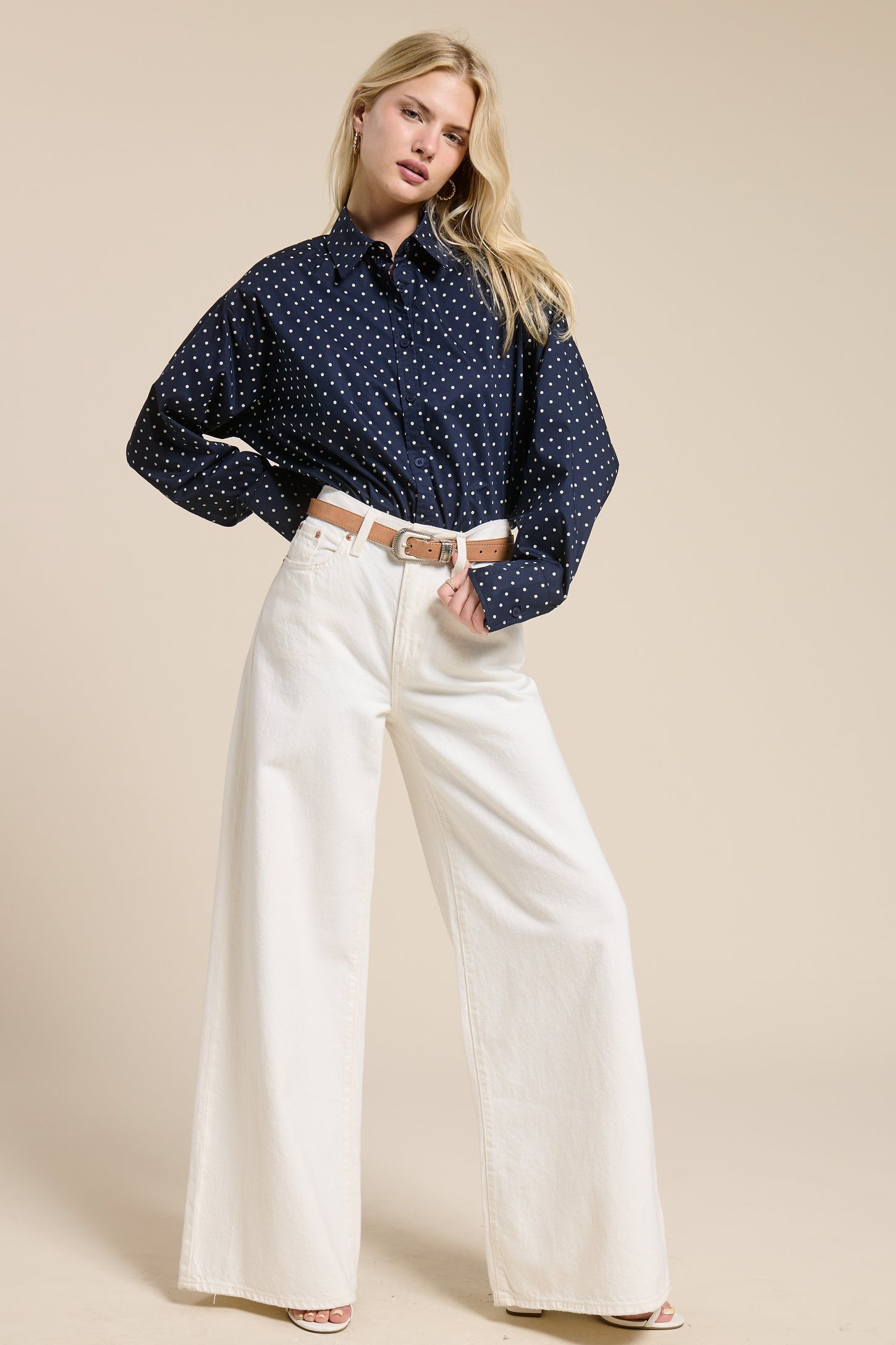 woman wearing a navy blue polka dot oversized shirt and white wide leg trousers
