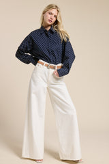 woman wearing a navy blue polka dot oversized shirt and white wide leg trousers