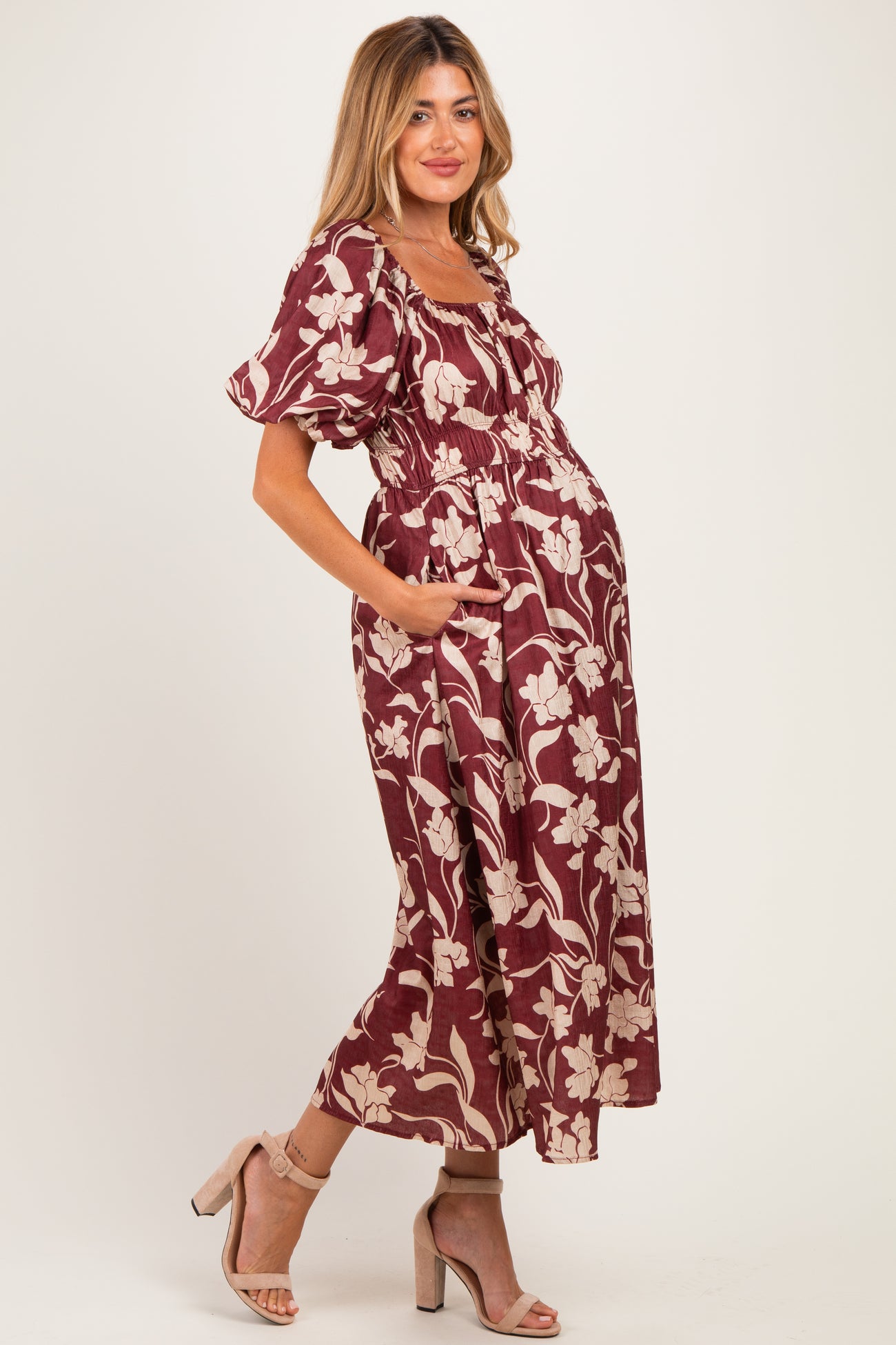 woman wearing a burgundy floral print maternity dress with puff sleeves and side pockets, showcasing a baby bump