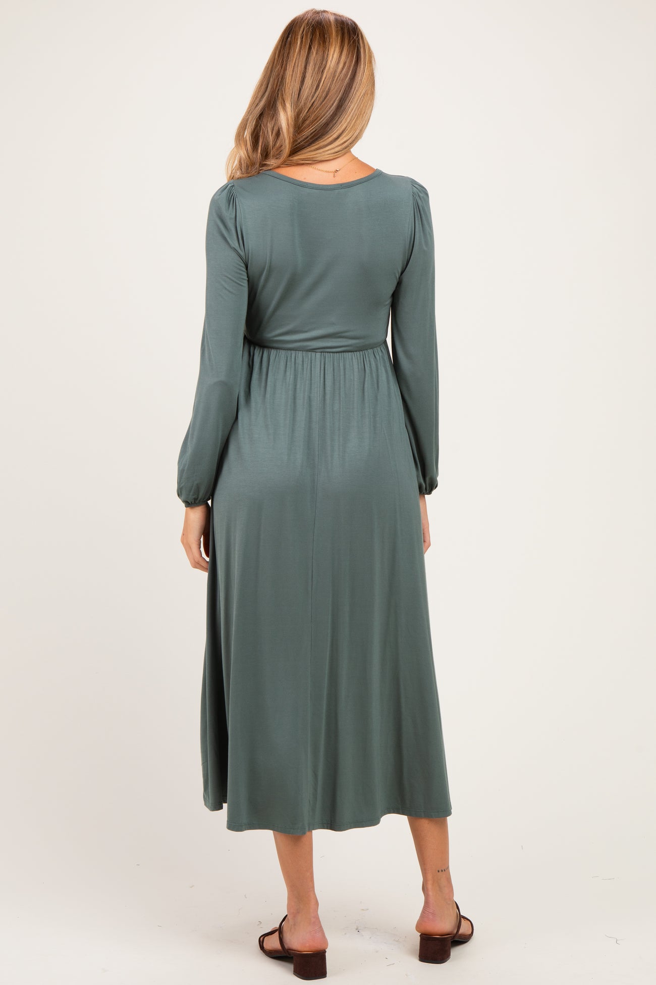 woman wearing a green maternity maxi dress with long sleeves and a fitted waist, showing a baby bump from the back