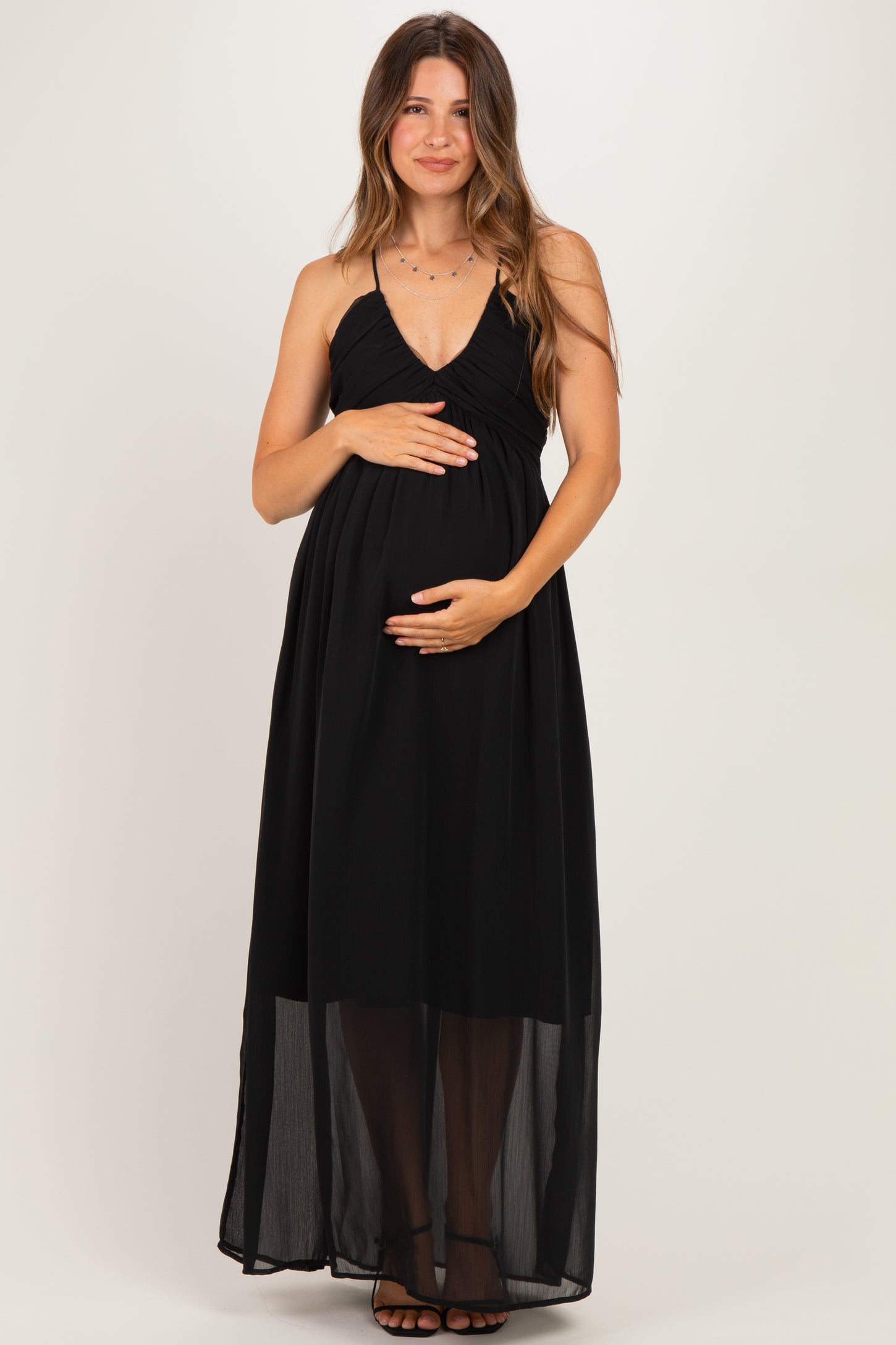 woman wearing a black maternity maxi dress with spaghetti straps and holding her baby bump