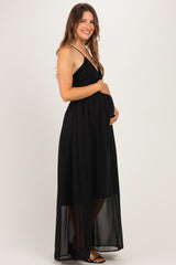 woman wearing a black maternity maxi dress with a sheer overlay and holding her baby bump