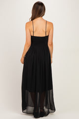 woman wearing a black maternity maxi dress with a smocked bodice and sheer overlay, showing the back view