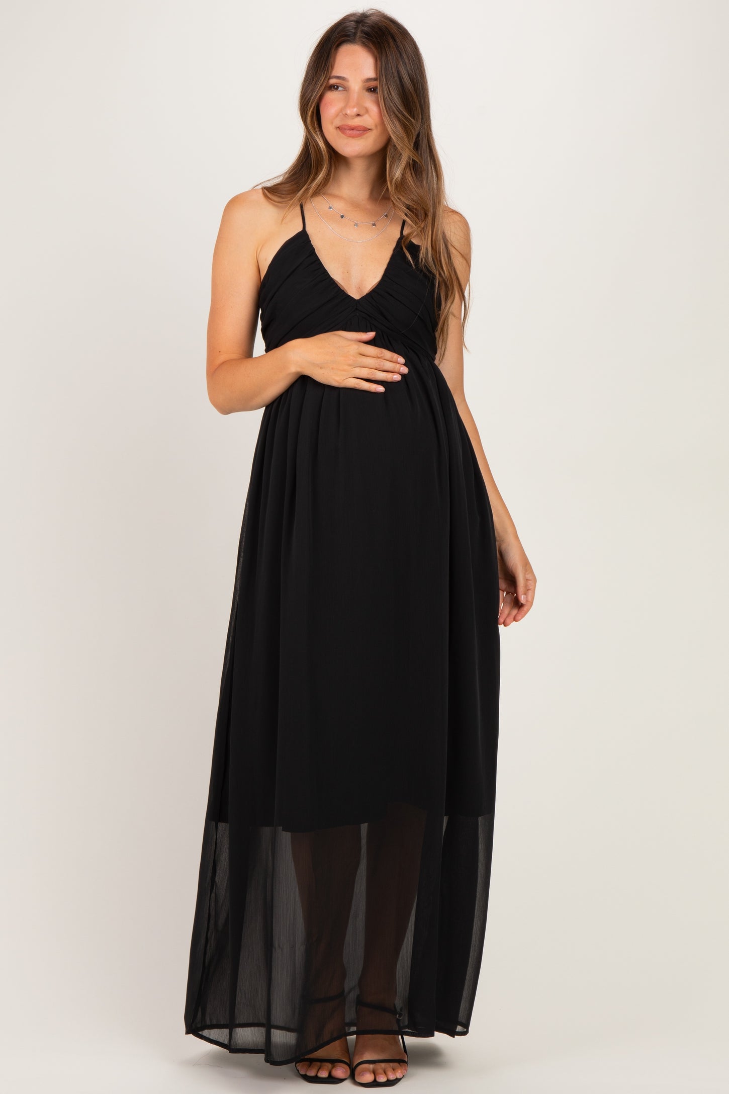woman wearing a black maternity maxi dress with a sheer overlay and holding her baby bump