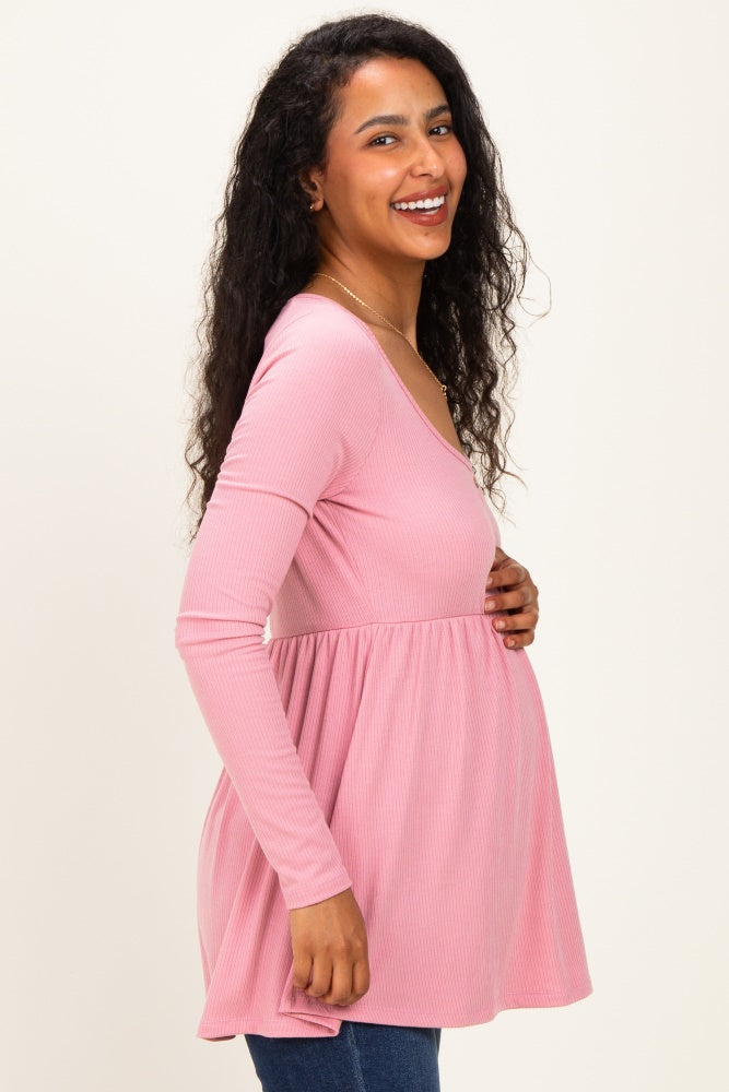 woman wearing a light pink long sleeve maternity top with a babydoll style, highlighting her baby bump