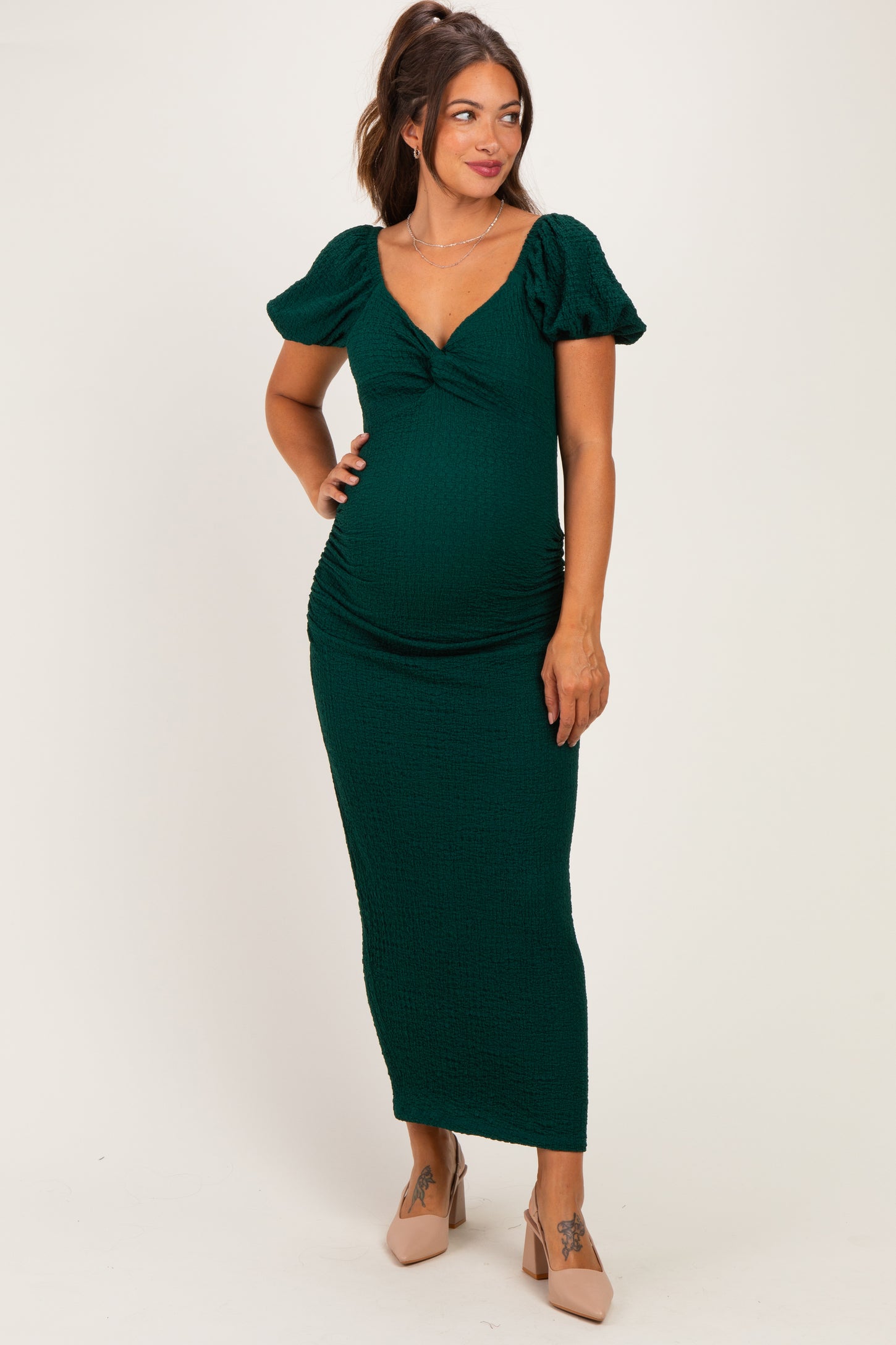 woman wearing a green maternity dress with puff sleeves and a ruched design, showing her baby bump