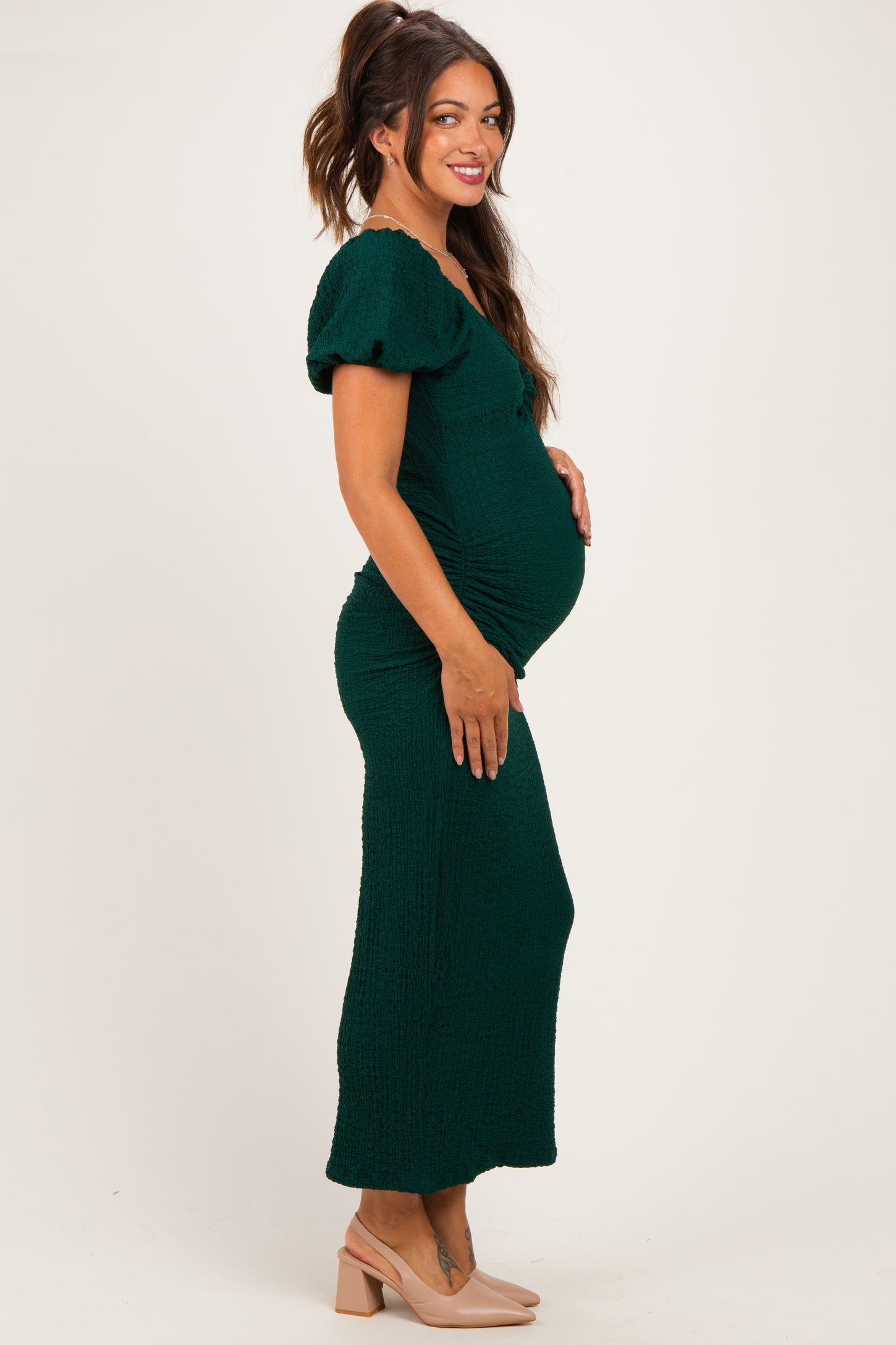 woman wearing a green maternity dress with puff sleeves and ruching, showing off her baby bump