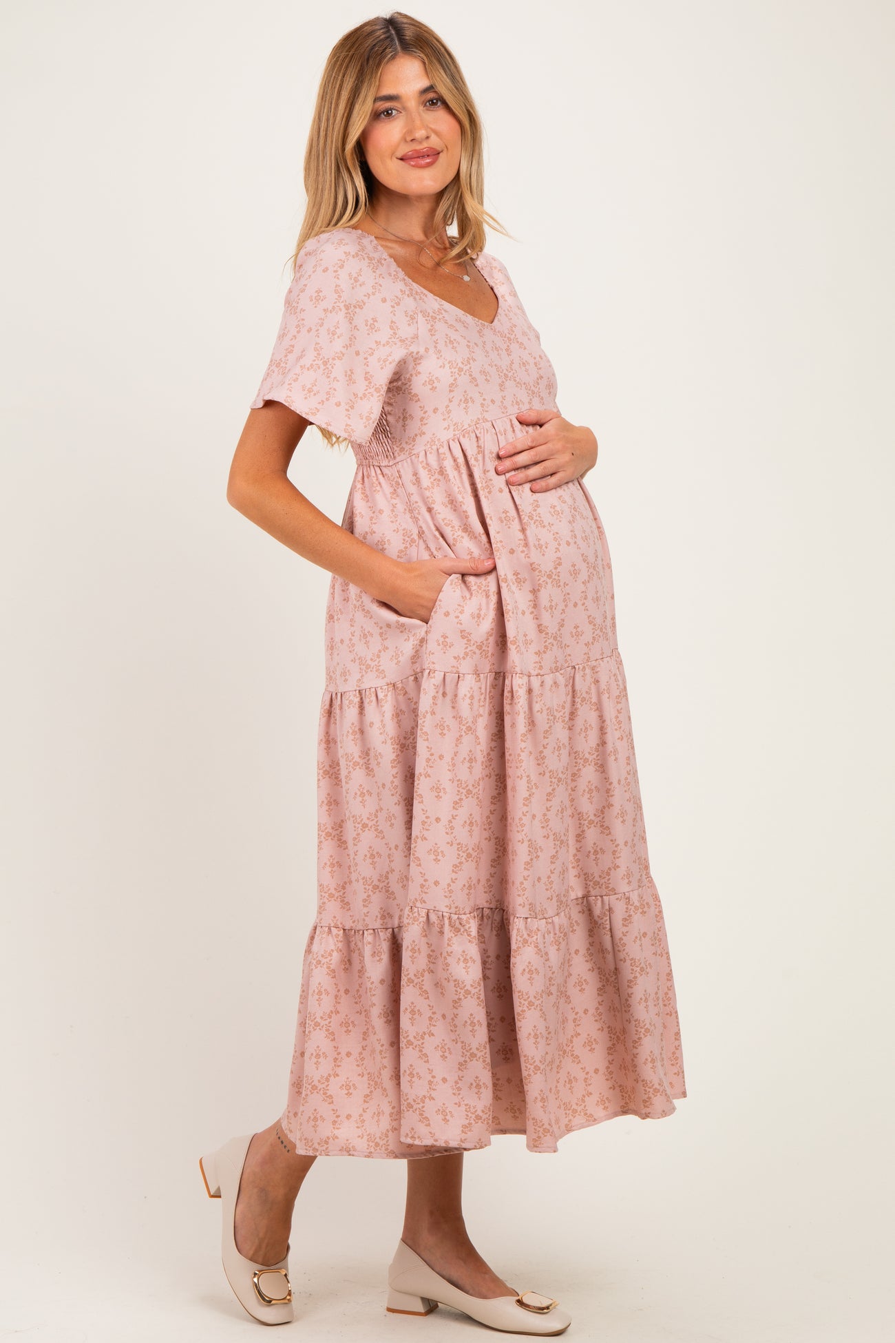 woman wearing a pink floral maternity dress with short sleeves and a tiered skirt, holding her baby bump