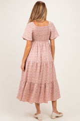woman wearing a pink floral maternity dress with short sleeves and a smocked bodice, showing a baby bump