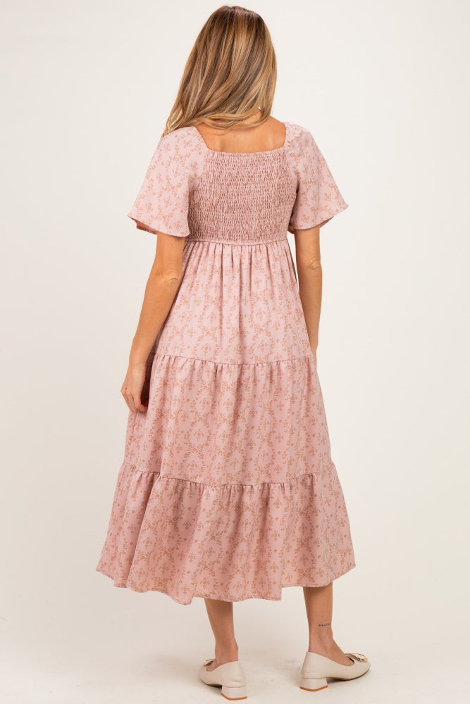 woman wearing a pink floral maternity dress with short sleeves and a smocked bodice, showing a baby bump