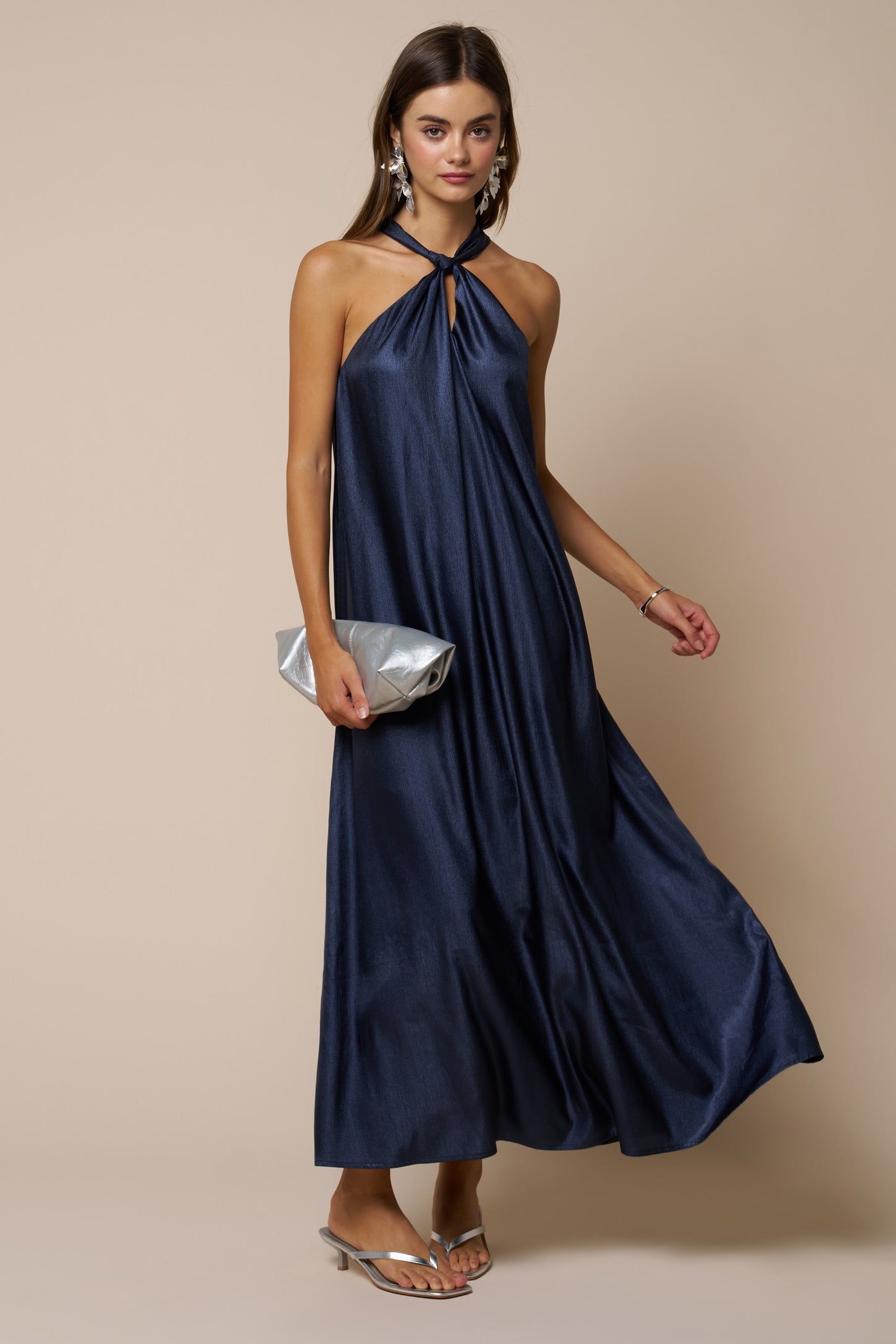 woman wearing a navy halter neck maxi dress with a front keyhole detail, holding a silver clutch purse