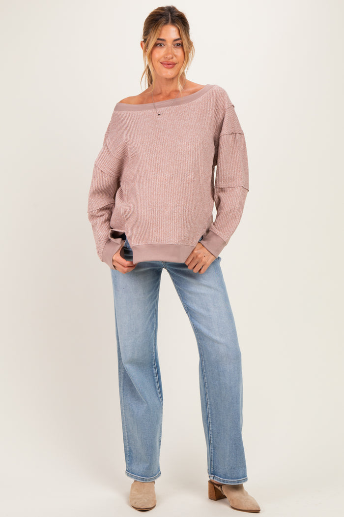 woman wearing a light pink off-the-shoulder maternity sweater and blue wide-leg jeans with a casual pose