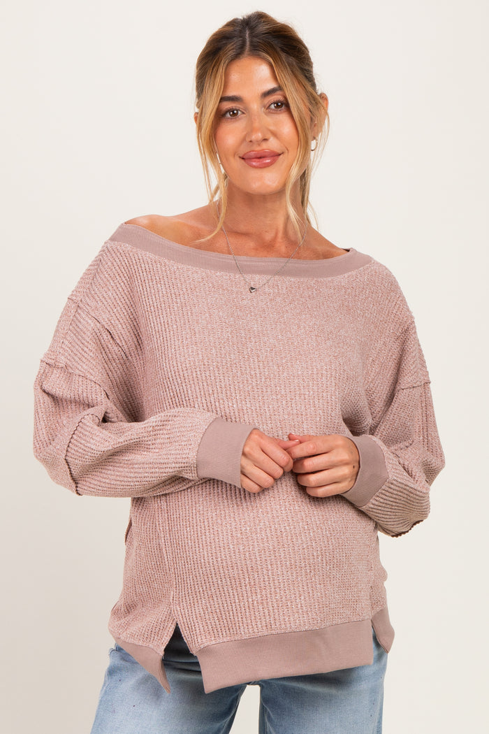 woman wearing a light pink oversized maternity sweater with boat neckline and ribbed texture, gently cradling her baby bump