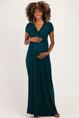 woman wearing a teal maternity maxi dress with a v-neck and short sleeves, holding her baby bump