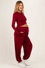 woman wearing a burgundy long sleeve maternity top and matching jogger pants, revealing baby bump with a relaxed fit