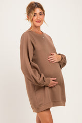 woman wearing a brown oversized maternity sweatshirt and gently cradling her baby bump