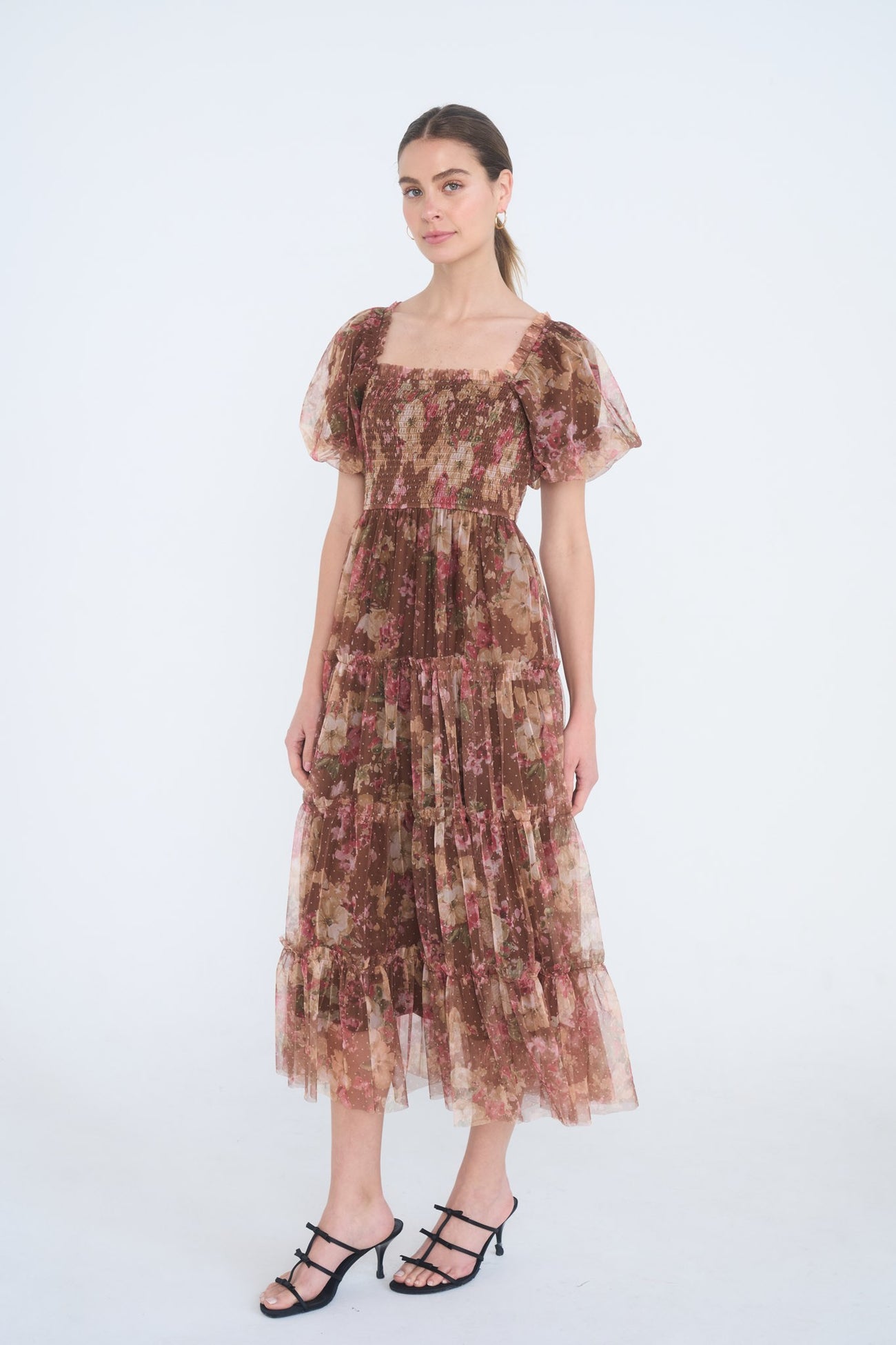 woman wearing a brown floral maxi dress with puff sleeves and tiered ruffles, standing against a white background