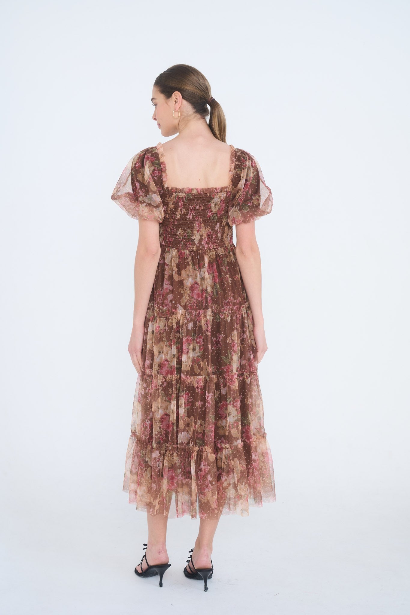 woman wearing a brown floral midi dress with puff sleeves and tiered ruffle hem, shown from the back