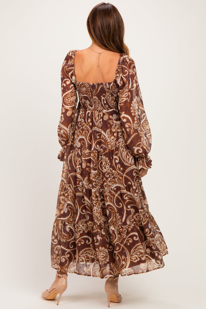 woman wearing a brown floral maxi dress with long sleeves and a tiered skirt, viewed from the back