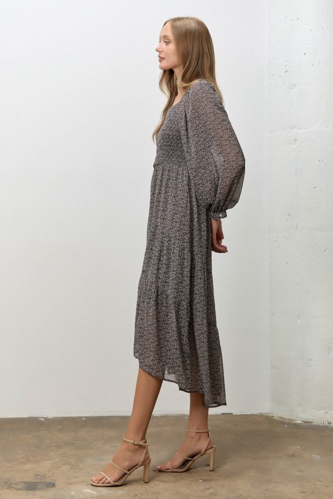 woman wearing a gray floral midi dress with long sleeves and tiered hem, paired with nude heeled sandals