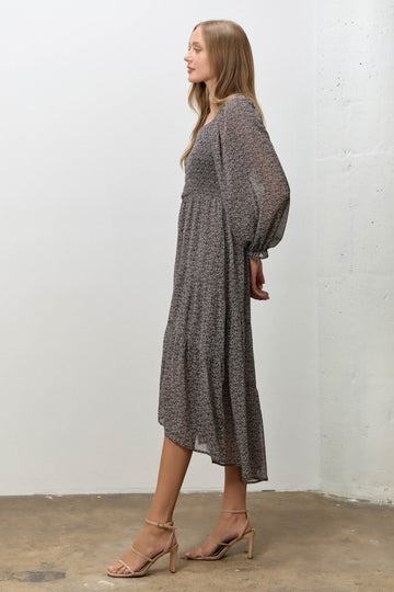 woman wearing a gray floral midi dress with long sleeves and tiered hem, paired with nude heeled sandals